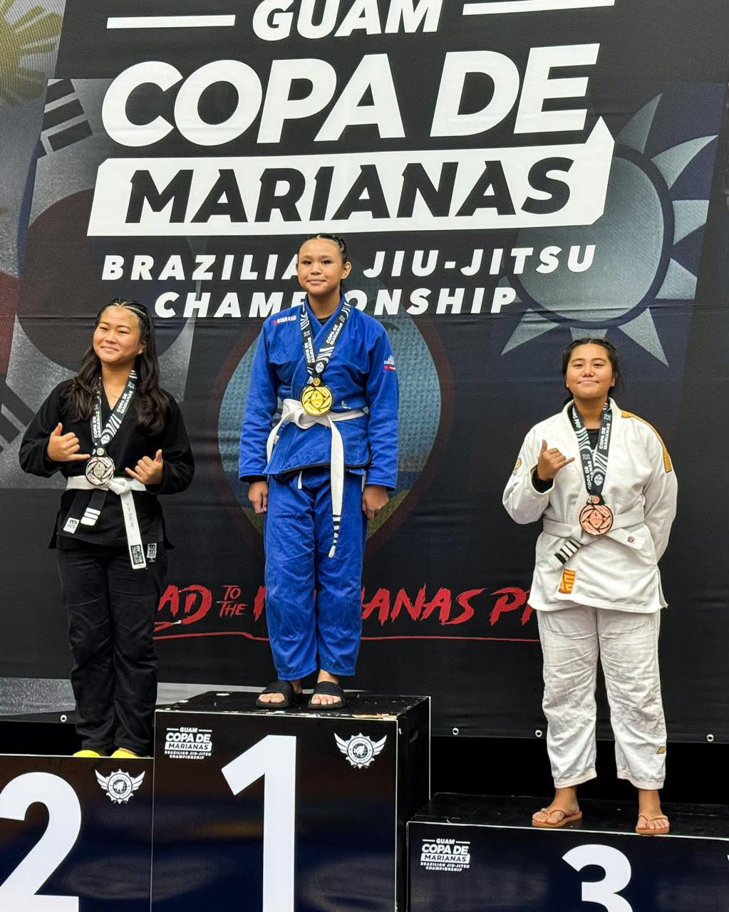 Sophia Miranda on the top of the Copa de Marianas podium in a blue gi with her gold medal